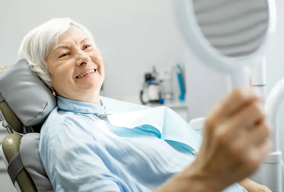 Female after getting dental implants looking at the mirror smiling